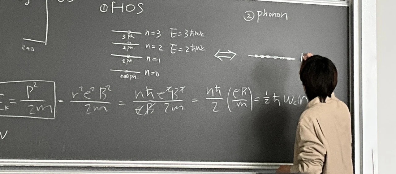 Xunyang teaching physics at a blackboard filled with equations.